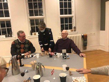 Et billede, der indeholder fire personer ved et bord. Der er kaffe, gaver og flag på bordet.