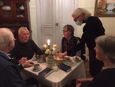 Et billede af fire personer siddende omkring et bord. Der er opdækning til kaffe og salmebøger på bordet.